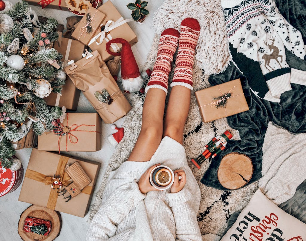 Crop faceless woman drinking tea and sitting near Christmas tree