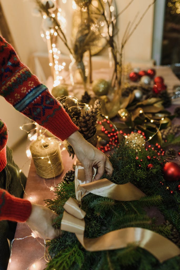 Close-up of hands decorating a Christmas wreath with ribbon and ornaments indoors.