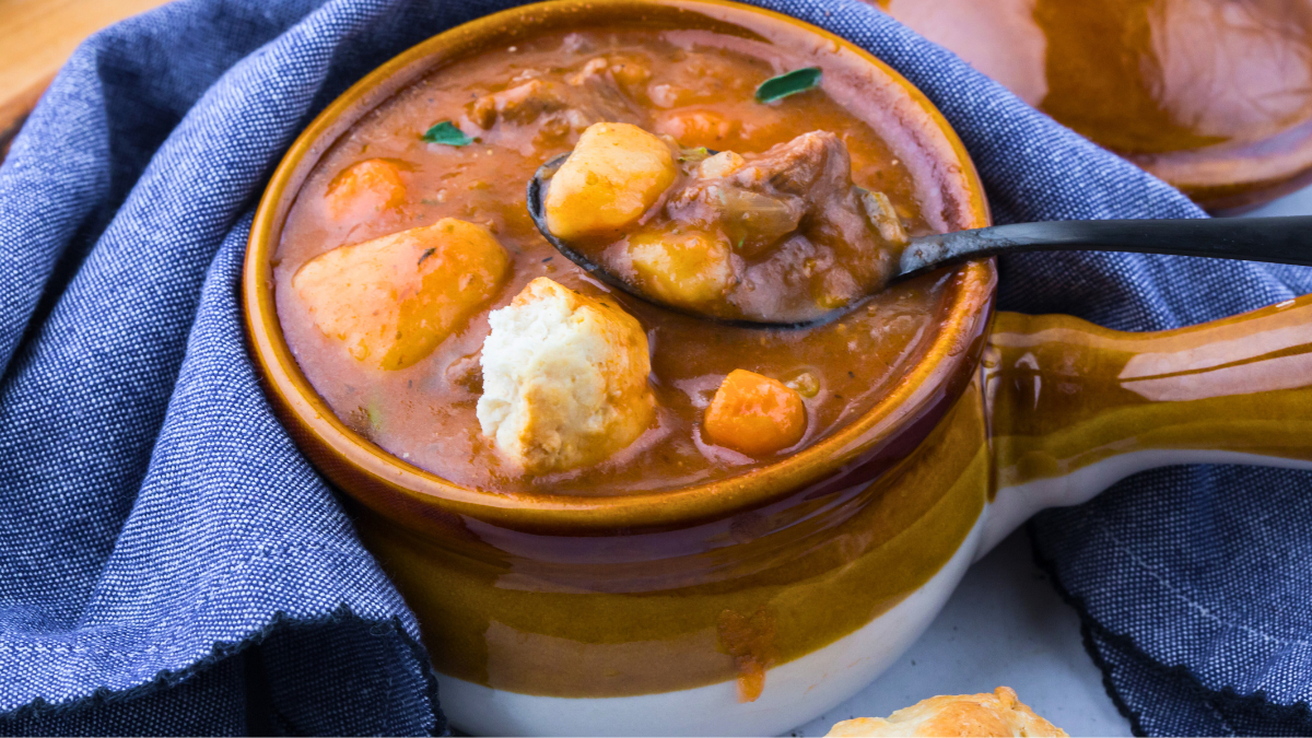 Close up beef stew in a soup bowl with a biscuit. Get the recipe for this classic beef stew cooked in the Instant Pot at DearCreatives.com